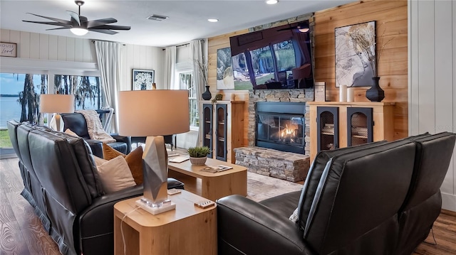 interior space with wooden walls, visible vents, ceiling fan, wood finished floors, and a stone fireplace