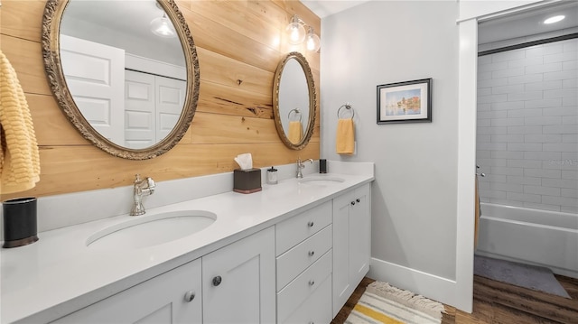 full bath with wood finished floors, a sink, wooden walls, and double vanity