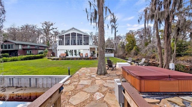 rear view of property with a sunroom, a hot tub, a patio area, and a yard