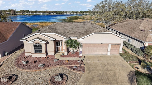 view of front facade with driveway, a water view, an attached garage, and stucco siding