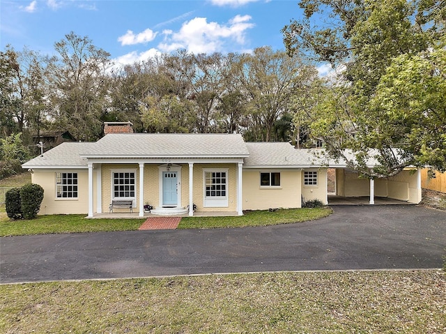 ranch-style home featuring a chimney, a shingled roof, covered porch, an attached carport, and driveway