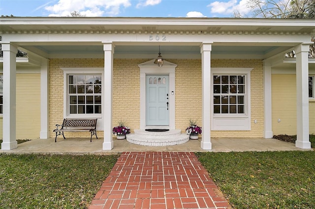 doorway to property featuring brick siding and a porch