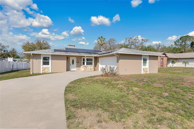 ranch-style home with a front yard, fence, driveway, a garage, and roof mounted solar panels