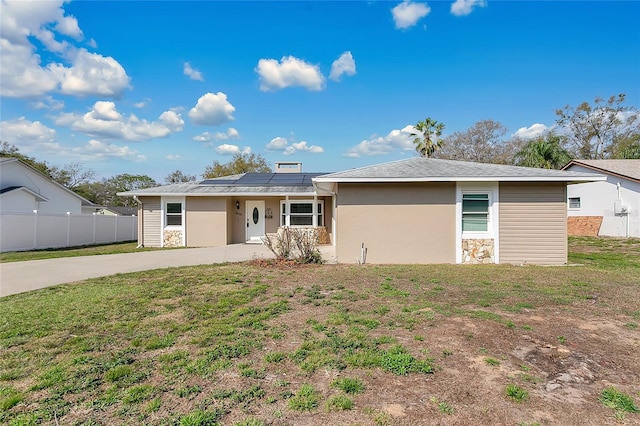 view of front of property with a front lawn, fence, roof mounted solar panels, and stucco siding