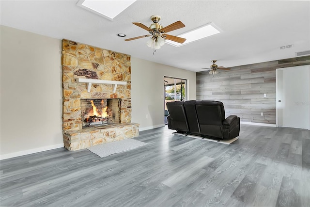 unfurnished living room featuring a fireplace, a skylight, an accent wall, and wood finished floors