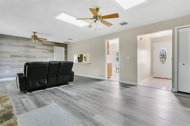 living area featuring visible vents, wood finished floors, a skylight, and an accent wall