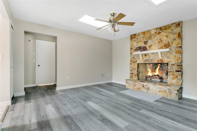 unfurnished living room featuring a stone fireplace, a skylight, baseboards, and wood finished floors