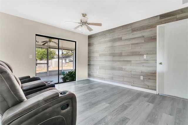 living room featuring wooden walls, baseboards, a ceiling fan, and wood finished floors