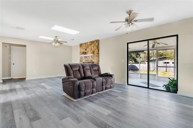 living area with visible vents, a ceiling fan, wood finished floors, a skylight, and baseboards