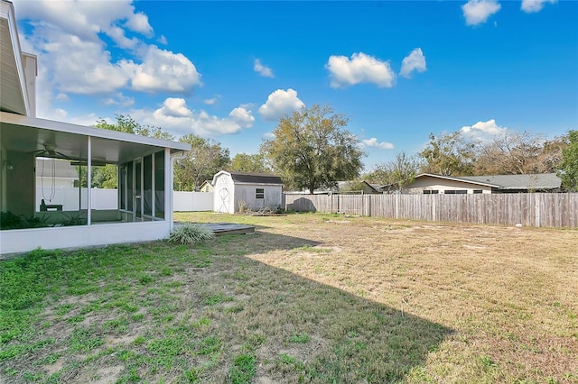 view of yard featuring an outbuilding, a storage shed, a fenced backyard, and a sunroom