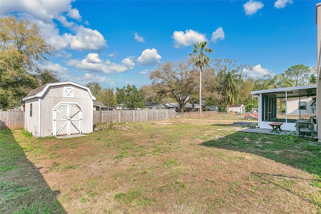 view of yard with a storage shed, a sunroom, a fenced backyard, and an outbuilding