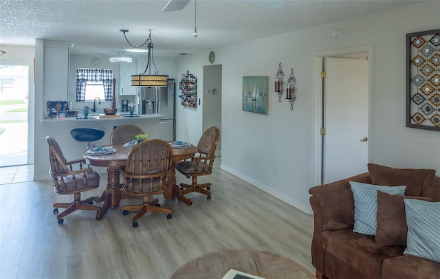 dining space featuring baseboards, light wood-style flooring, and a textured ceiling