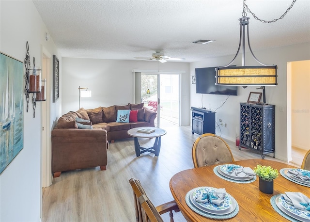 dining space featuring a textured ceiling, visible vents, light wood-style flooring, and a ceiling fan