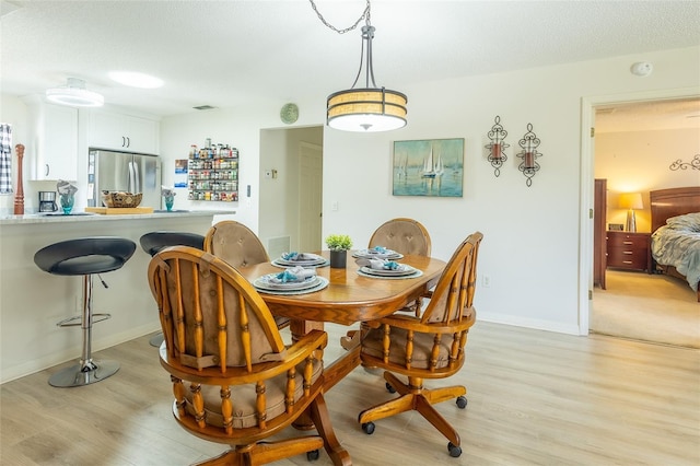 dining room with a textured ceiling, light wood finished floors, visible vents, and baseboards