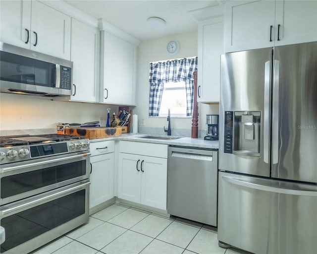 kitchen with light tile patterned floors, appliances with stainless steel finishes, a sink, and white cabinetry