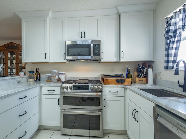 kitchen featuring light stone counters, light tile patterned floors, appliances with stainless steel finishes, white cabinetry, and a sink