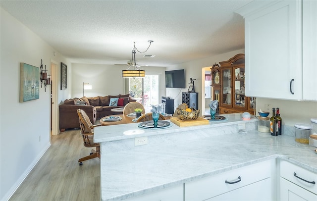 kitchen with open floor plan, a peninsula, light stone countertops, and white cabinets