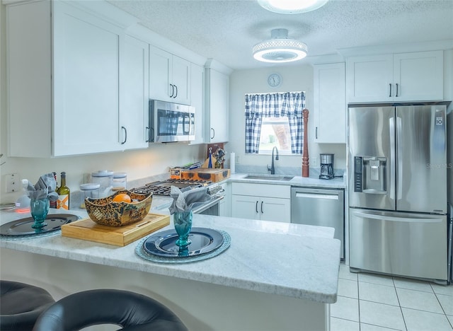 kitchen with light stone counters, light tile patterned floors, appliances with stainless steel finishes, white cabinetry, and a sink