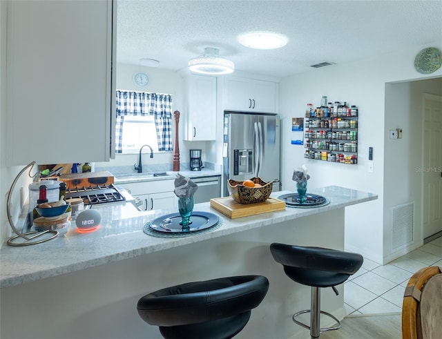 kitchen with stainless steel refrigerator with ice dispenser, a sink, visible vents, and white cabinetry