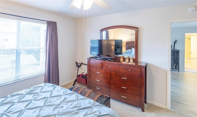 bedroom with ceiling fan, baseboards, a textured ceiling, and light colored carpet