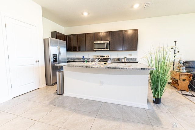 kitchen with light tile patterned floors, dark brown cabinetry, visible vents, appliances with stainless steel finishes, and light stone countertops