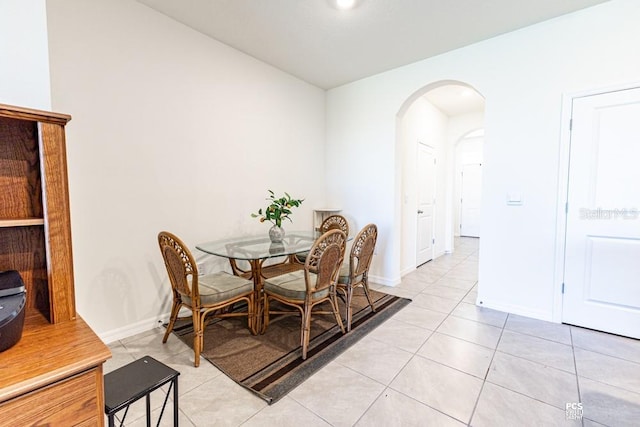 dining room featuring arched walkways, light tile patterned flooring, and baseboards