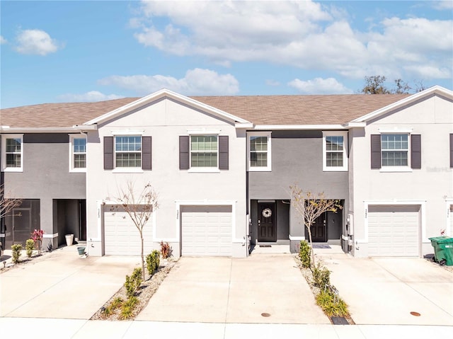 townhome / multi-family property featuring a shingled roof, driveway, an attached garage, and stucco siding