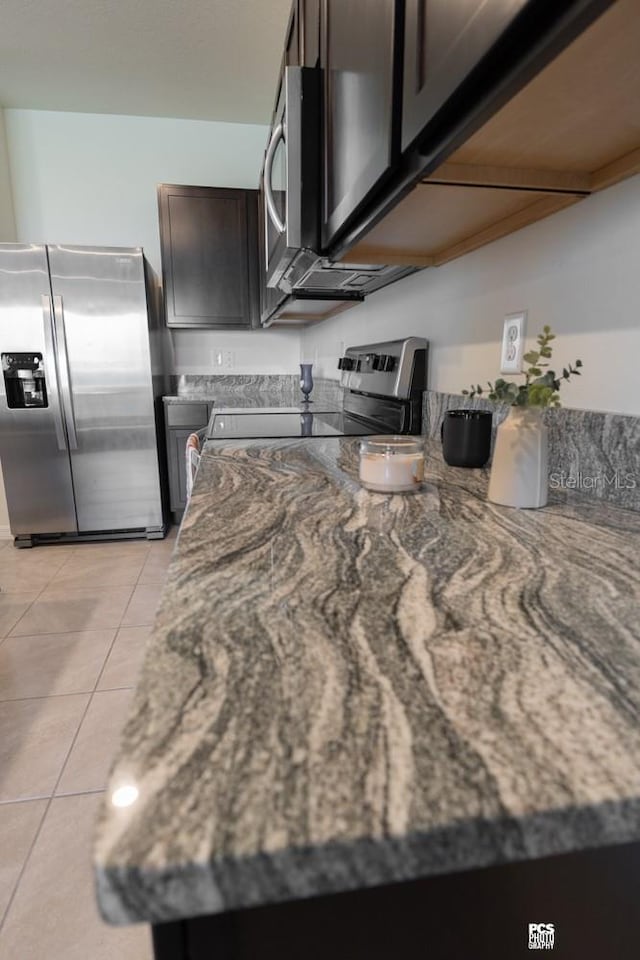 kitchen featuring light tile patterned floors, stone counters, appliances with stainless steel finishes, and dark brown cabinets