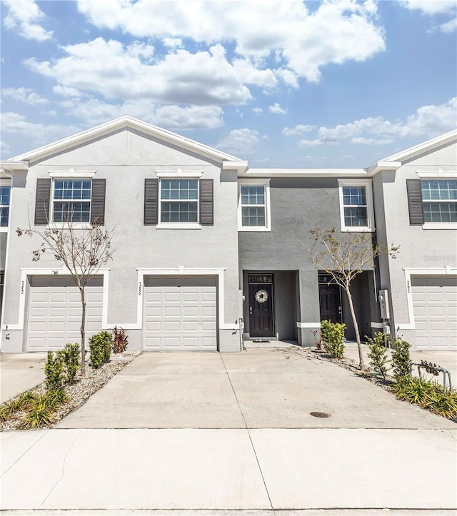 townhome / multi-family property with a garage, concrete driveway, and stucco siding