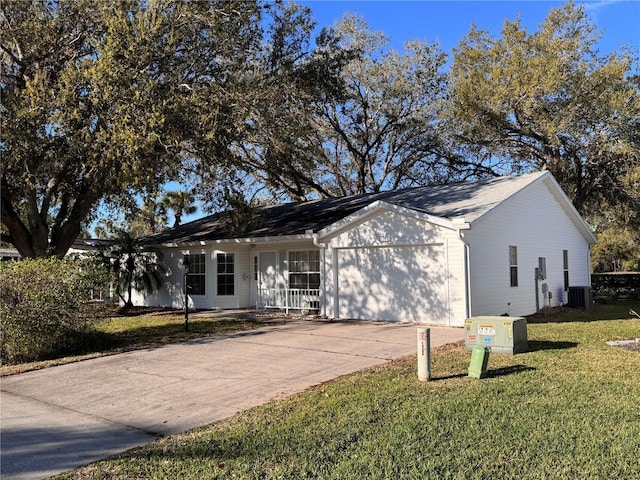 ranch-style home featuring an attached garage, driveway, a front lawn, and central AC unit