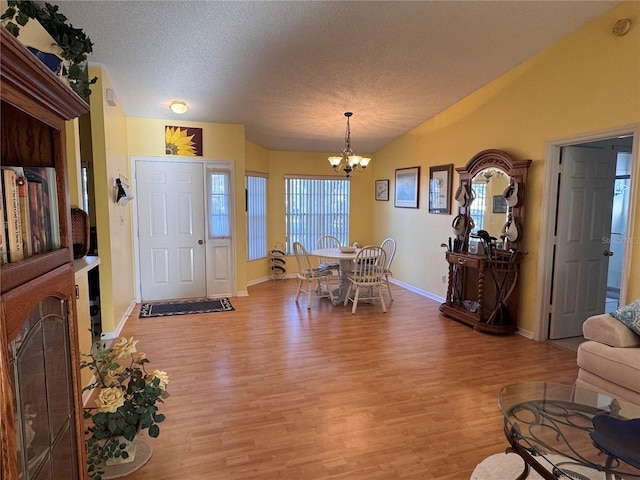 foyer with a textured ceiling, a chandelier, light wood-style flooring, baseboards, and vaulted ceiling