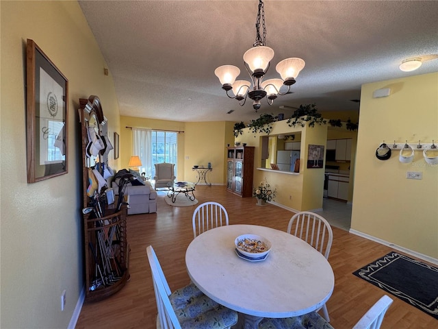 dining space featuring wood finished floors, a textured ceiling, baseboards, and an inviting chandelier