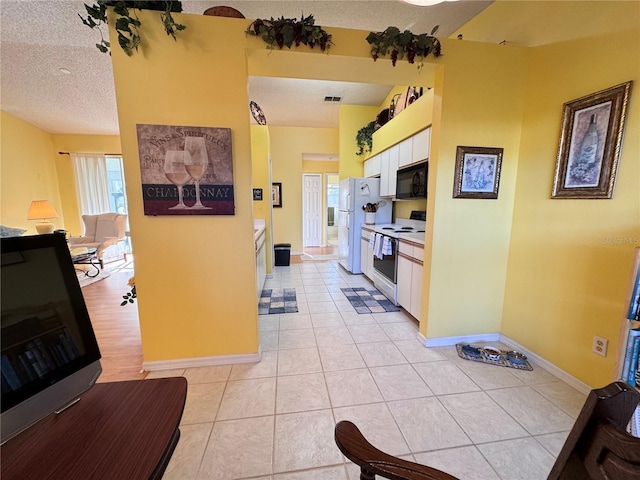 kitchen featuring a healthy amount of sunlight, white appliances, white cabinetry, and a textured ceiling