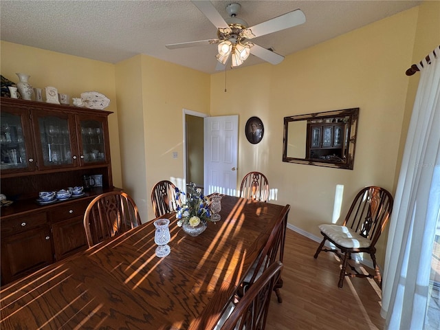 dining area featuring a ceiling fan, a textured ceiling, baseboards, and wood finished floors