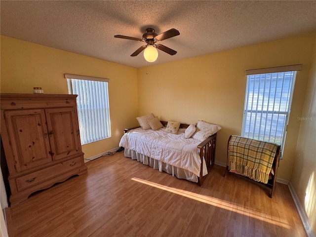 bedroom with light wood-style floors, a ceiling fan, baseboards, and a textured ceiling