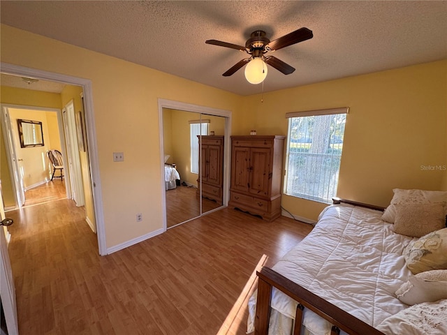 bedroom with baseboards, ceiling fan, wood finished floors, a textured ceiling, and a closet