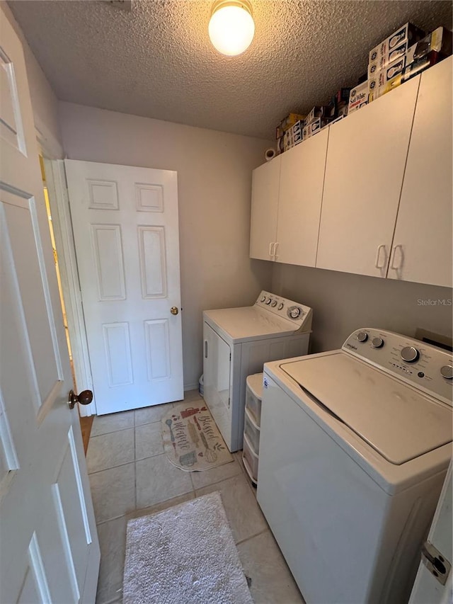 laundry area with cabinet space, light tile patterned floors, separate washer and dryer, and a textured ceiling