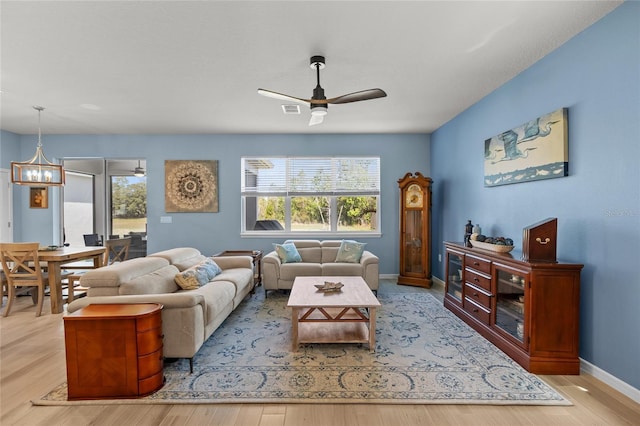 living room featuring ceiling fan with notable chandelier, wood finished floors, visible vents, and baseboards