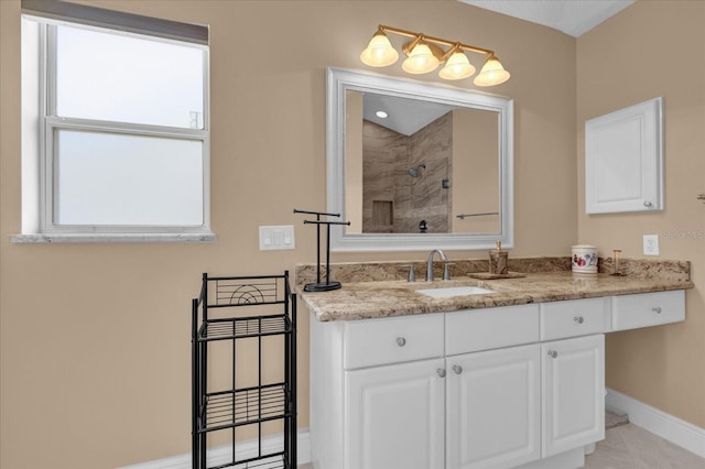 full bathroom with baseboards, tiled shower, and vanity