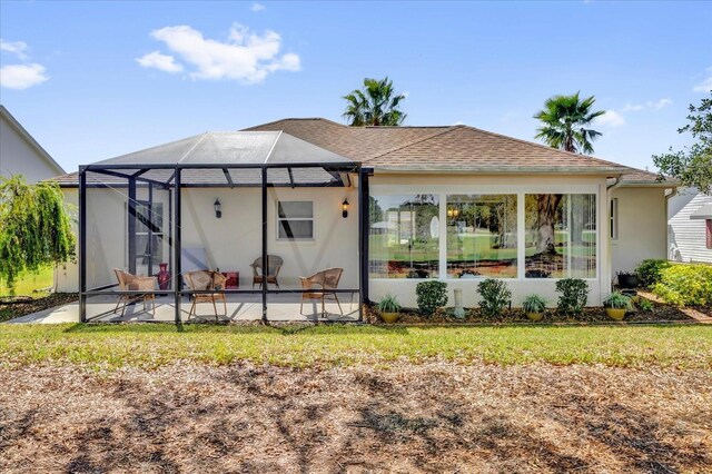 rear view of property with glass enclosure, roof with shingles, and a patio