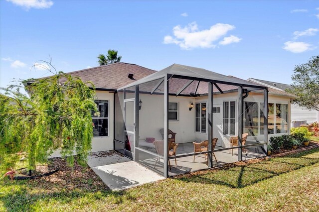 rear view of property with a patio, stucco siding, a shingled roof, a lawn, and a lanai