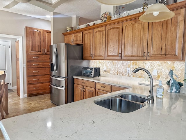 kitchen with decorative backsplash, stainless steel fridge, a sink, and brown cabinets