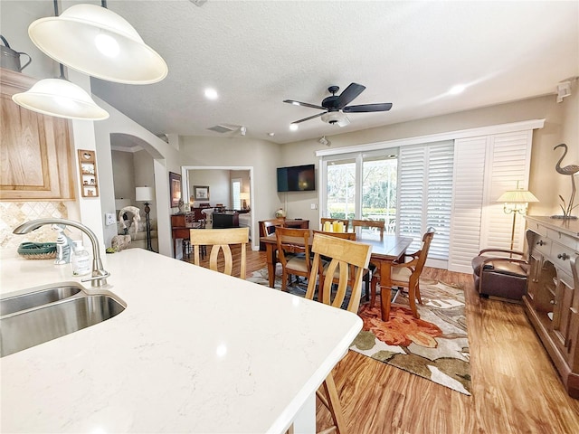 kitchen featuring arched walkways, decorative backsplash, light countertops, light wood-style floors, and a sink