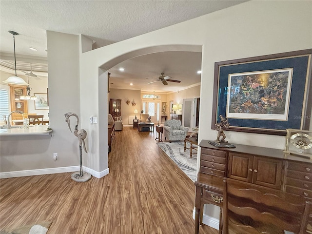 hall featuring baseboards, arched walkways, wood finished floors, a textured ceiling, and recessed lighting