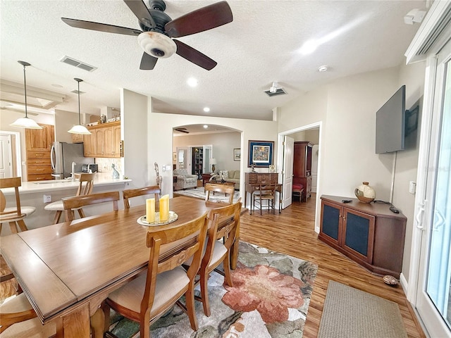 dining room featuring light wood-type flooring, arched walkways, visible vents, and a textured ceiling