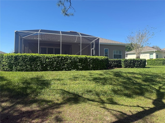 rear view of house featuring a lanai, a lawn, and stucco siding