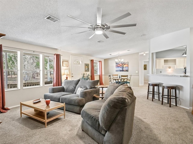 living room with ceiling fan with notable chandelier, visible vents, a textured ceiling, and light colored carpet