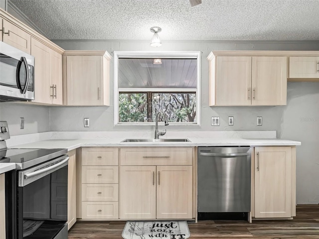 kitchen featuring a textured ceiling, stainless steel appliances, a sink, light brown cabinetry, and dark wood finished floors