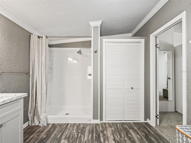 full bath with a textured ceiling, wood finished floors, vanity, ornamental molding, and a stall shower