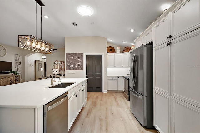 kitchen with lofted ceiling, arched walkways, a sink, stainless steel appliances, and white cabinets